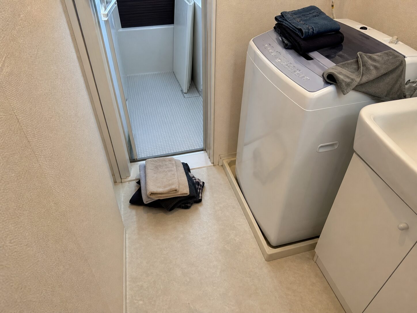 狭い脱衣所の床と洗濯機上に着替えが置かれて動線が狭くなった状態