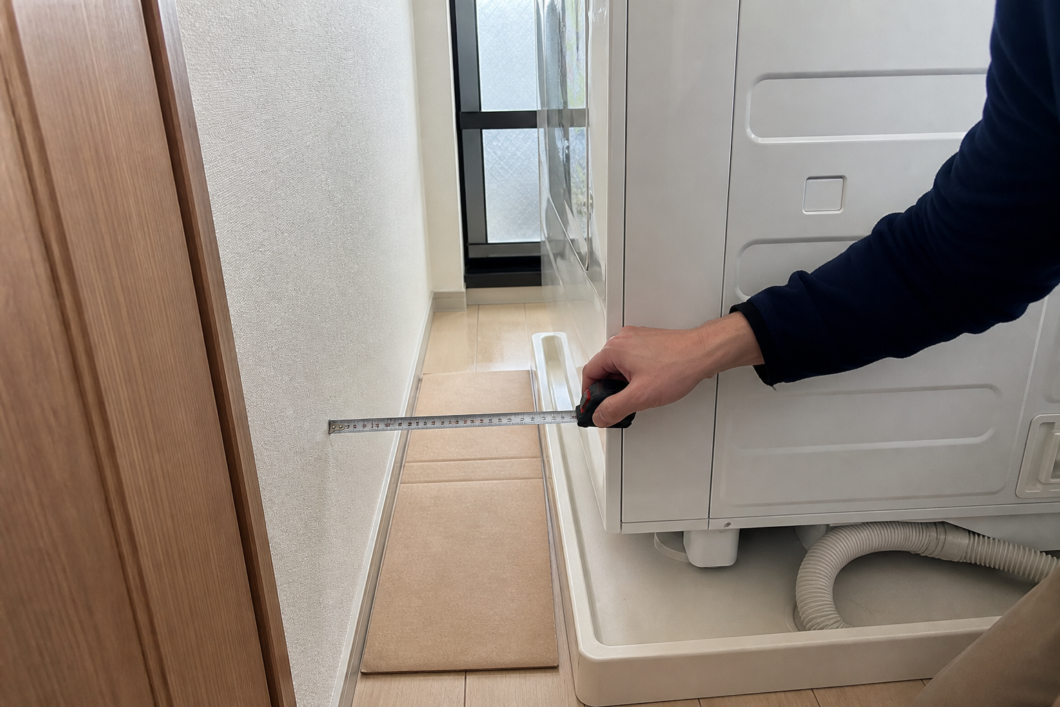 洗濯機横の防水パンとホースがあるすき間を測っている様子